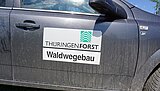 Linkziel: Link zum Beitrag mit dem Thema Waldwegeinstandsetzung nach Schadflächensanierung ; Bildinhalt: Eine Fahrzeugseite mit ThüringenForstaufkleber und der Aufschrift Wegebau.