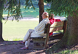 Seniorenpärchen im Wald auf einer Bank an einem See.