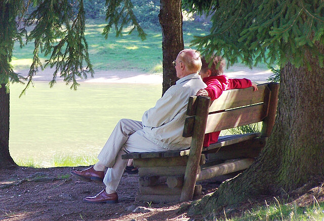 Seniorenpärchen im Wald auf einer Bank an einem See.