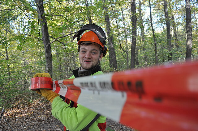 Ein Waldarbeiter sichert einen Bereich im Wald mit Absperrband.