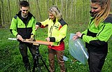 Zwei junge Frauen und ein junger Mann in Dienstkleidung von ThüringenForst stehen euf einer Waldlichtung und werten eine entnommene Bodenprobe aus