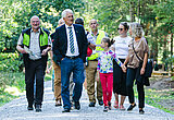 Linkziel: Link zum Beitrag mit dem Thema Familienfest am Stausee Hohenfelden hat voll gepunktet; Bildinhalt: Kleine Gruppe von Personen läuft auf einem Waldweg durch einen grünen Sommerwald.